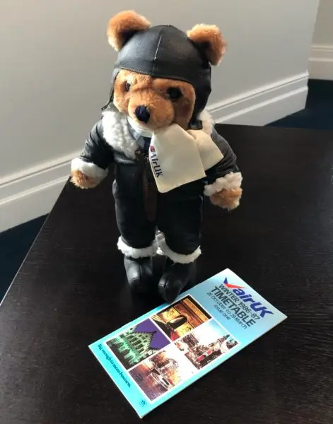 Colour photo of Air UK teddy bear dressed in pilot's uniform, with Air UK printed timetable