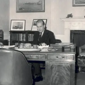 Black and white photograph of Sir Nicholas Cayzer, 2nd Bart., of Roffey Park (as he was then) at his desk in the St. Mary Axe office.